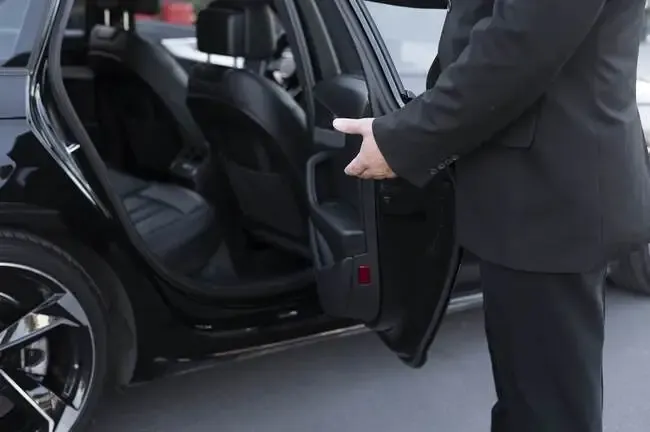 Chauffeur privé en costume élégant ouvrant la portière d'une Mercedes noire pour un client