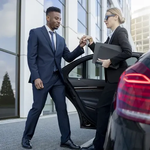 Chauffeur privé en costume élégant bleu ouvrant la portière d'une Mercedes noire pour une cliente