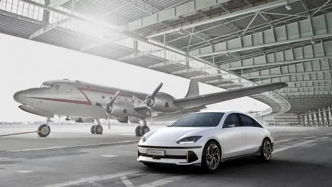 Véhicule moderne garé dans un hangar aéroportuaire près d'un avion vintage à hélices
