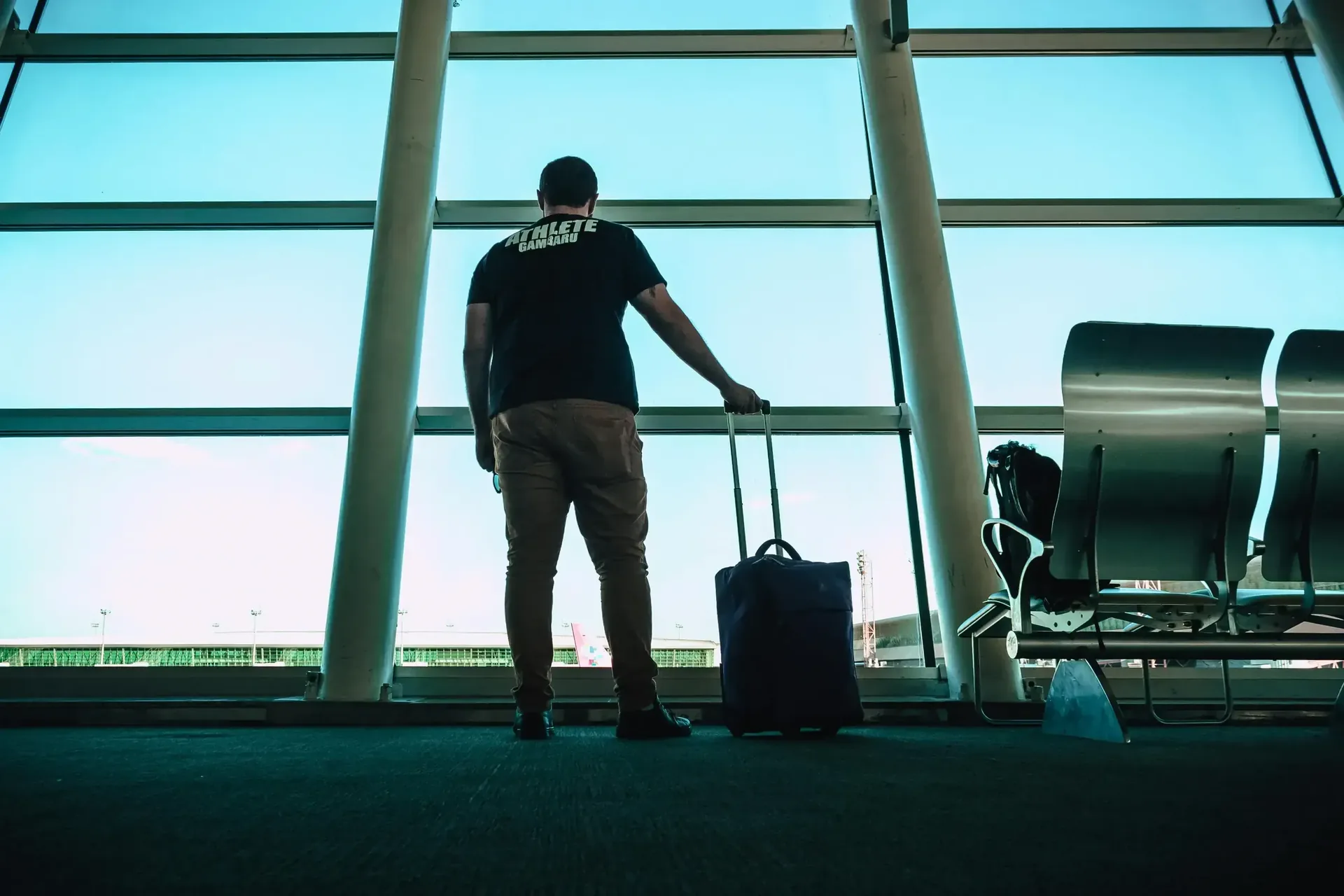 Homme avec une valise attendant près d'une fenêtre à l'aéroport, prêt pour un départ en VTC vers sa destination