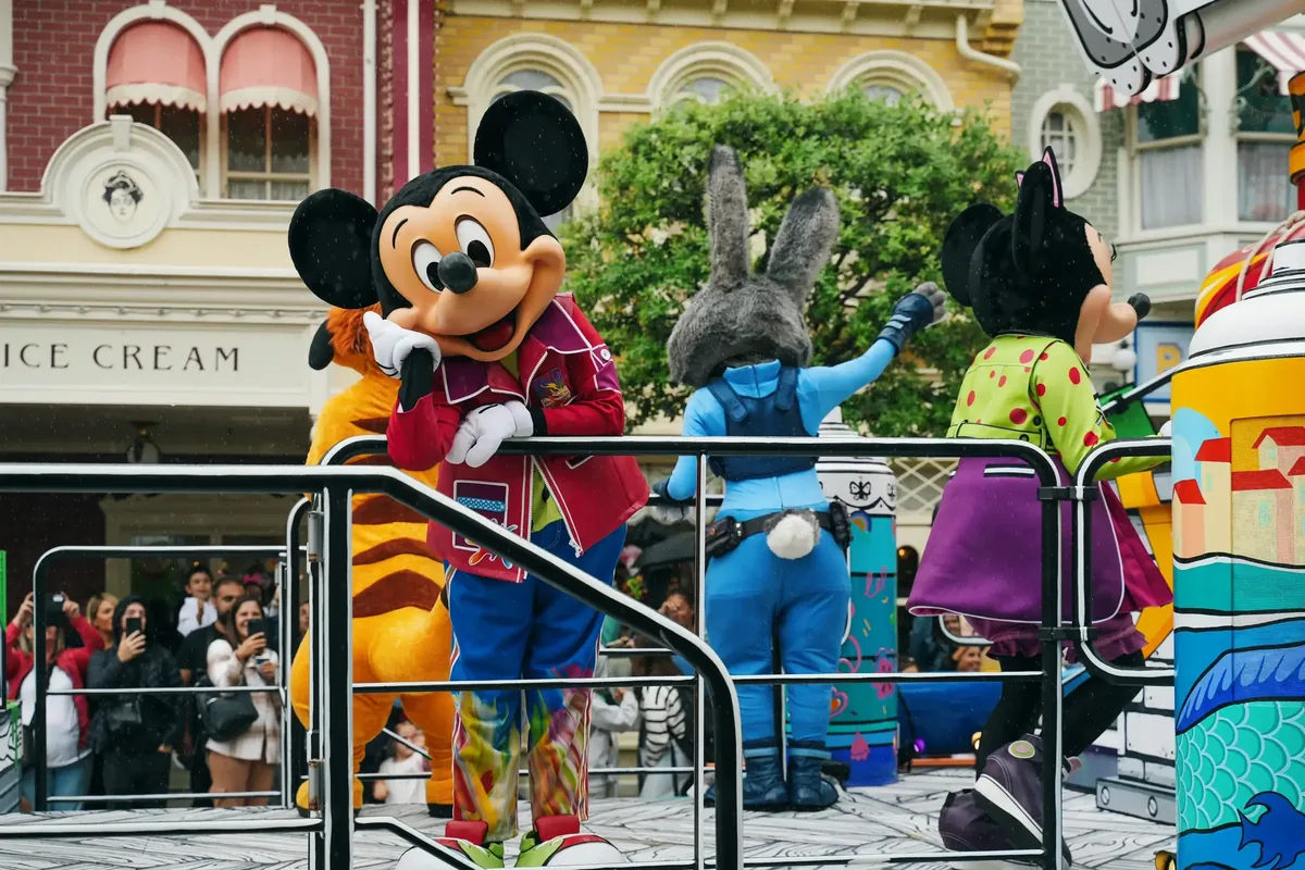 Personnages Disney incluant Mickey Mouse et Minnie dans une parade à Disneyland Paris, entourés de visiteurs prenant des photos