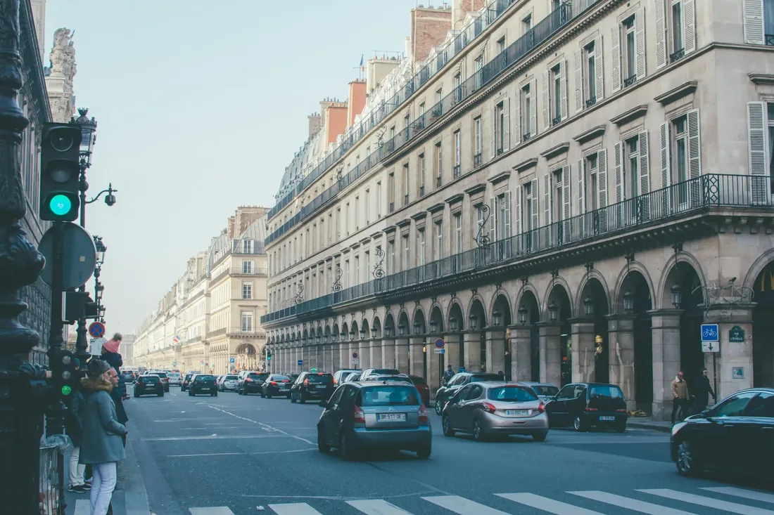Rue parisienne animée avec ses immeubles haussmanniens, ses arcades et la circulation