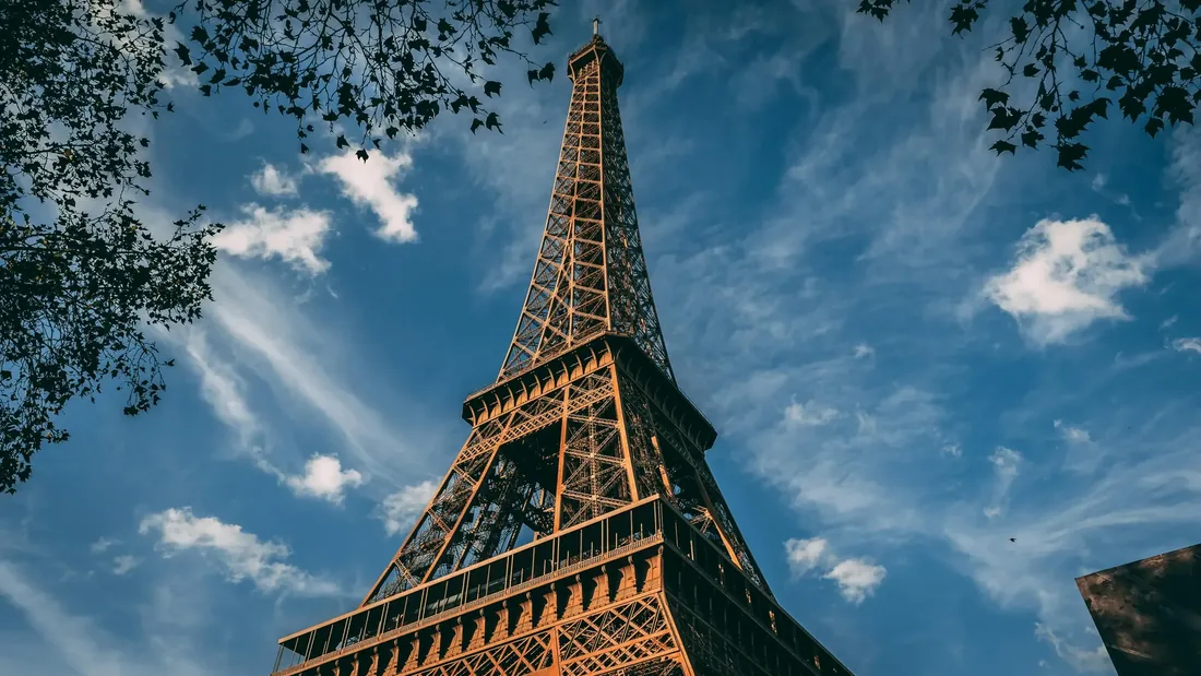 Tour Eiffel vue en contre-plongée à travers les branches d'arbres, sous un ciel bleu