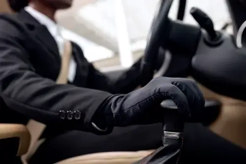 Chauffeur privé en costume noir portant des gants noirs, tenant le levier de vitesse d'une voiture VTC