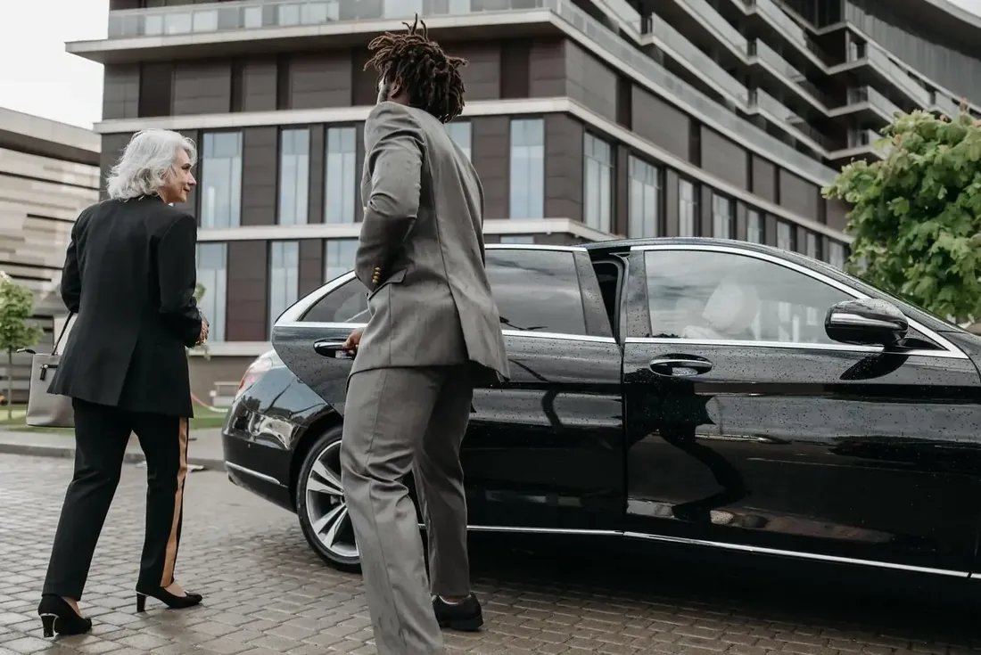 Chauffeur en costume gris ouvrant la porte d'une Mercedes noire à une cliente